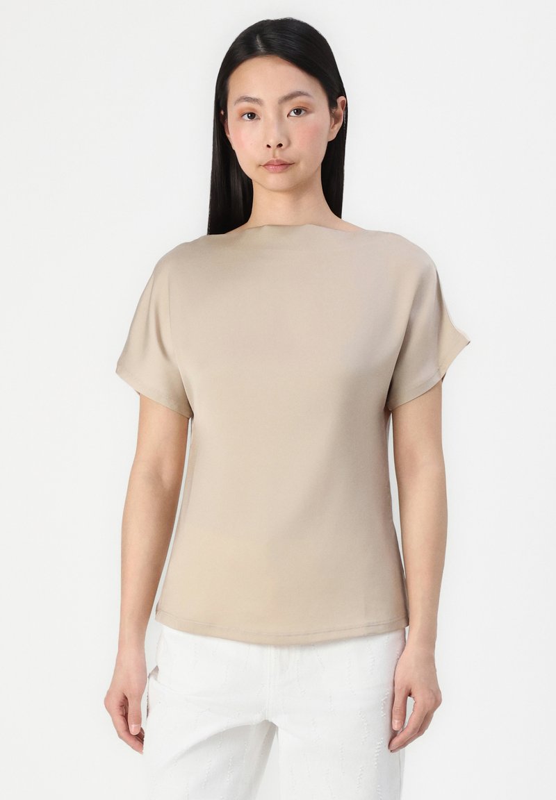 Haut beige à manches courtes avec un col bateau et un tissu lisse et léger. Présente une coupe décontractée et un léger éclat.