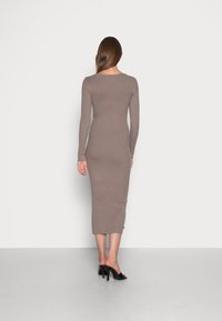 Pitkähihainen, ribbineulottu mekko taupe-värissä, istuva siluetti, polvipituus, sileä tekstuuri. Yhdistetty mustiin korollisiin mule-kenkiin.