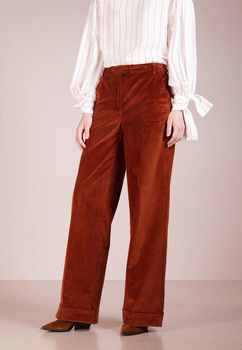 Brązowe kordurojowe spodnie o szerokich nogawkach z miękką fakturą i podwiniętymi mankietami, zestawione z paskowaną bluzką z długim rękawem.