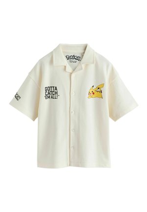 Kremfarvet kortærmet skjorte med knapper med teksten "GOTTA CATCH 'EM ALL!" og Pikachu-grafik på fronten samt Pokémon-logo på ærmet.