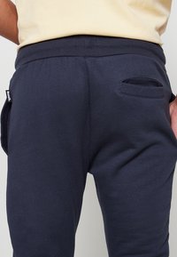 Marineblauwe sweatpants met een geribde tailleband en een klein achterzakje. Gemaakt van zachte stof met een gladde textuur. Bench-logo label zichtbaar.