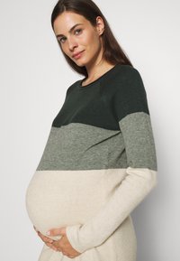 Strikket mammasweater med fargeblokkdesign i mørk grønn, lys grå og krem. Lange ermer, rund hals, myk tekstur.