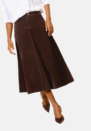 Woman wearing a dark brown A-line midi skirt and brown pointed-toe heels with a white long-sleeve shirt.
