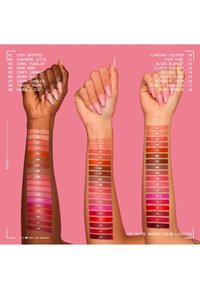 Trois bras avec différentes teintes de peau montrent 18 échantillons de rouges à lèvres mats allant des nudes clairs aux rouges profonds sur un fond rose.