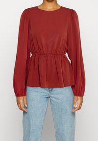 Bordó dlouhý rukáv blůza s kulatým výstřihem, nařaseným pasem a balónovými rukávy. Hladká tkanina s mírně strukturovaným povrchem. V kombinaci s modrými džíny.