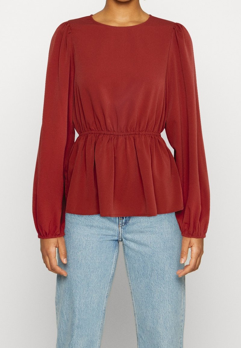 Bordó dlouhý rukáv blůza s kulatým výstřihem, nařaseným pasem a balónovými rukávy. Hladká tkanina s mírně strukturovaným povrchem. V kombinaci s modrými džíny.