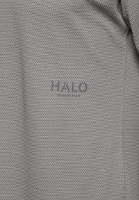 Szary materiał o fakturze z widocznym szwem oraz logo "HALO" nadrukowanym ciemnymi literami blisko środka.