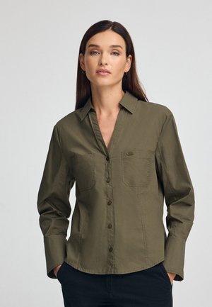 Camicia verde oliva a maniche lunghe con bottoni, realizzata in tessuto leggero, con colletto e due tasche frontali. Texture liscia.