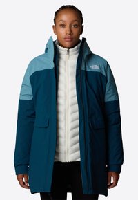 Isoleret parka med en mørk teal farve og lys blå detaljer, en hvid indre lag, lynlås lukning og forlommer.