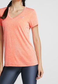 Camiseta de manga corta con escote en V en color coral rosa jaspeado, hecha de una tela suave, con un pequeño logo gris en el pecho.