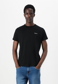 T-shirt in cotone nero con maniche corte e collo rotondo. Presenta un piccolo logo bianco sul petto. Abbinato a jeans in denim blu.