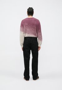 Sveter z vlnenej zmesi v prechode od fialovej po krémovú, s okrúhlym výstrihom a voľnými rukávmi; doplnený čiernymi cargo nohavicami s bočnými vreckami.