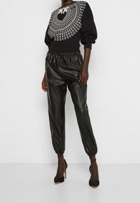 Černá mikina s grafickým motivem na límci, kombinovaná s černými tepláky z umělé kůže s elastickými lemy a černými lodičkami se špičatou špičkou.