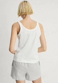Hvid bomulds tanktop med brede stropper, parret med grå og hvid stribede shorts. Blød tekstur, afslappet design, ingen synlige mønstre eller udsmykninger.