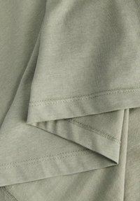 Zielona bawełniana tkanina z widocznymi fałdami i nakładającymi się warstwami. Charakteryzuje się gładką fakturą oraz widocznym przeszyciem wzdłuż brzegów.