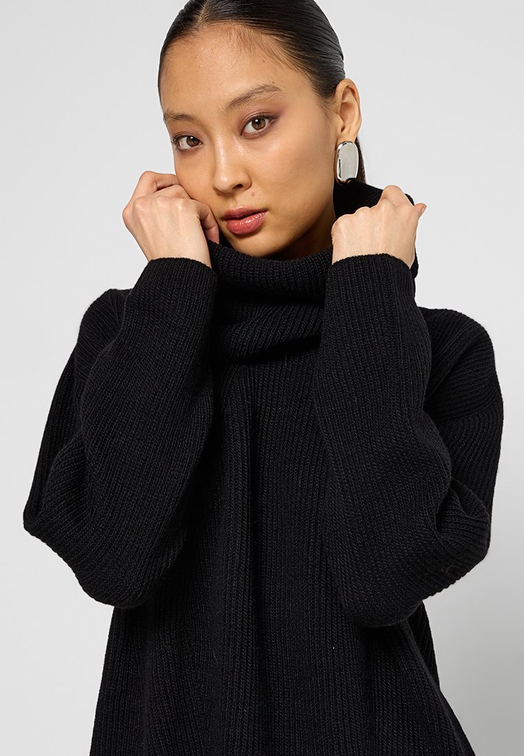 Schwarzer gerippter Rollkragenpullover mit lockerer Passform, breiten Ärmeln und hohem Kragen. Glatte Textur und gemütliches Aussehen.