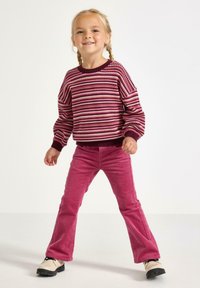 Strikket sweater i bordeaux, pink og creme striber; ribbede manchetter. Tætsiddende pink corduroy bukser og creme sko med sorte såler.