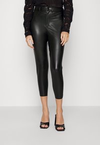 Černé kožené kalhoty s vysok�ým pasem a zkrácenou délkou, nošené s černými lodičkami s otevřenou špičkou na vysokém podpatku a topem s dlouhým rukávem z krajky.