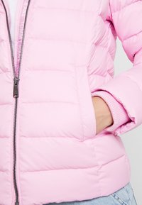 Padded rosa Jacke aus glattem Stoff, mit einem Reißverschluss vorne, gerippten Bündchen und seitlichen Taschen. Leichtes Design mit horizontalen Nähten.