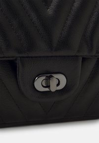 Borsa in pelle nera con motivo a zigzag trapuntato, dotata di una chiusura metallica rotonda. La texture è liscia e il colore è uniforme.