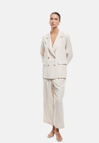 Lichtbeige dubbelzijdige blazer met grote knopen, gecombineerd met wijde broekspijpen. Gladde stof met een relaxte pasvorm en minimalistisch design.