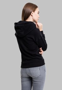 Svart hettegenser med teksturert overflate og justerbar snor i hetta, sammen med grå slim-fit jeans, sett fra siden og bak.