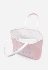 Sac fourre-tout en toile rose avec poignées synthétiques blanches, arborant un logo bleu et une poche intérieure zippée, texture lisse, design minimaliste.