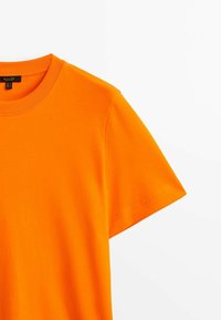 T-shirt di cotone arancione brillante con scollo rotondo e maniche corte, caratterizzato da una texture liscia e una costruzione pulita.