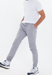 Helle graue Jogginghosen mit elastischen Bündchen und Seitentaschen, kombiniert mit einem weißen T-Shirt und mehrfarbigen Sport-Sneakern.