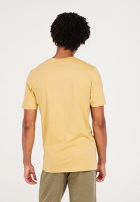 Korte mouw, ronde hals t-shirt van lichtgele katoen. Glad textuur, ontspannen pasvorm. Achteraan is een eenvoudige weergave zonder patronen of accenten.