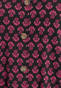 Tessuto nero con un motivo floreale rosa, caratterizzato da bottoni in legno lungo la parte anteriore. La texture è leggermente rigata con un design costante.