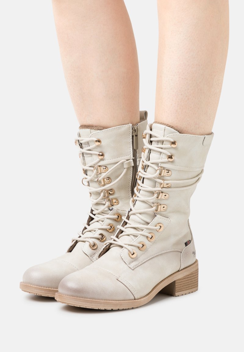 Lace-up ankle boots in soft light beige leather with a rounded toe, gold hardware, side zip closure, and a stacked heel.