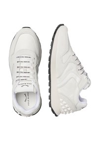 Sneaker bianche realizzate con materiali in suede e pelle, dotate di una suola in gomma nera testurizzata, lacci evidenti e un accento triangolare sul tallone.