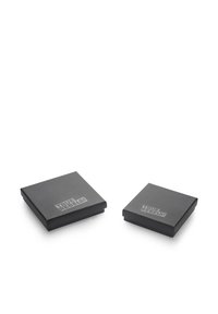 Črne kvadratne škatle z mat zaključkom, s povišanim napisom "PRAVI UPORNIKI!" na pokrovu, postavljene ena ob drugi. Kompaktna zasnova.