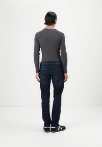Camisa de manga larga gris, textura acanalada, combinada con jeans de mezclilla azul oscuro. Diseño sencillo, corte recto y detalles en el bolsillo trasero.