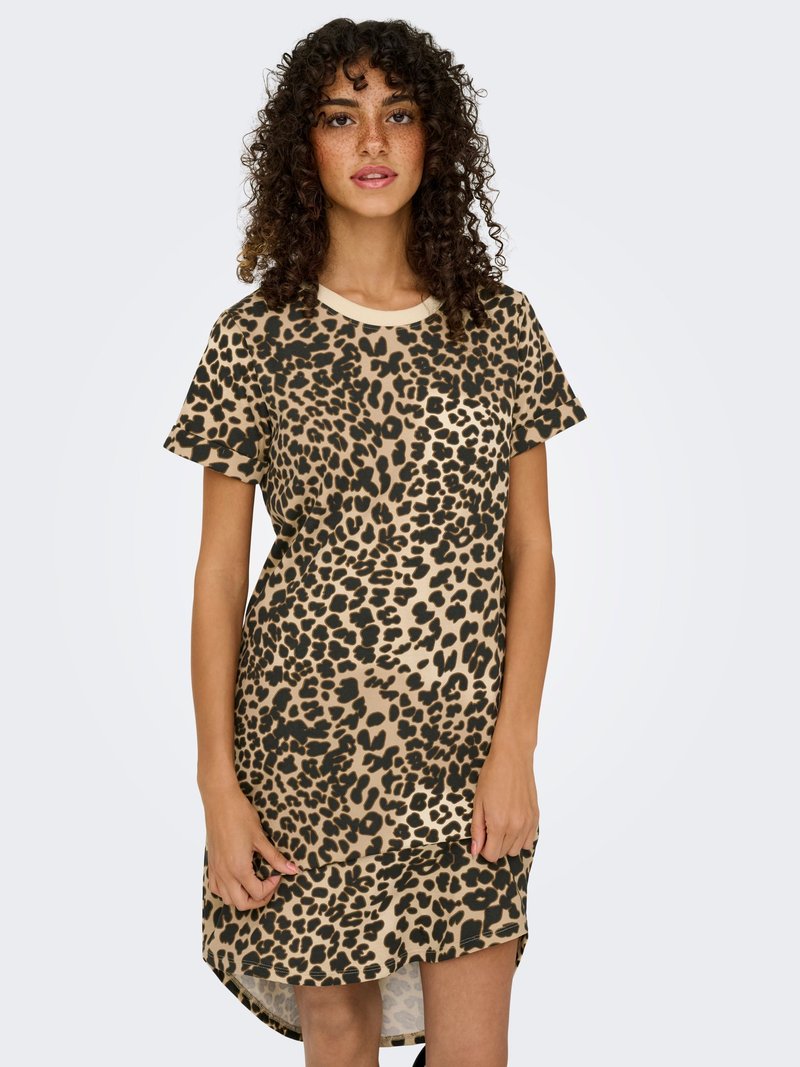 Kvinde med krøller iført en kortærmet kjole med leopardprint, stående mod en lys baggrund.