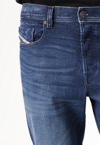 Jeans en denim bleu foncé avec un léger délavage, poche avant avec une étiquette décorative, fermeture à bouton en métal et un design classique droit.