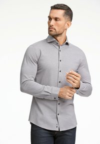 Maglietta grigia a maniche lunghe con un design a bottoni, bottoni neri e una silhouette aderente, abbinata a jeans in denim scuro. Tessuto dalla superficie liscia.