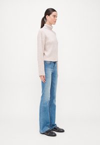 Pull à col roulé côtelé beige clair, longueur cropped, associé à un jean flare bleu clair et des chaussures à enfiler noires à clous.