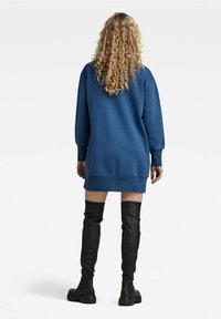 Blå oversized sweatshirtklänning med långa ärmar, ribbade manschetter och nederkant; ihop med åtsittande svarta lårhöga läderstövlar.