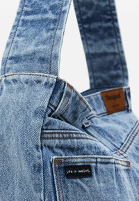 Denim-Tote mit blauer Nuance, ausgestattet mit gestickten Nähten, einem Lederetikett und einem schwarzen Aufnäher mit der Aufschrift "LIFE IS AWESOME."