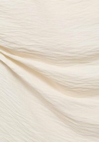 Tissu crème texturé avec des motifs ondulés subtils et une finition douce, présentant une apparence légère et légèrement froissée.