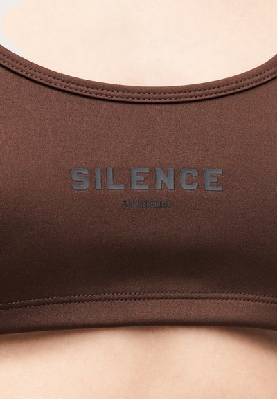 Barna sportmelltartó, sima textúrával, lekerekített nyakkivágással és a középen sötétszürkével nyomtatott „SILENCE” logóval.