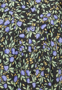 Svart tyg med ett blommönster som har lila blommor, gröna blad och gula accenter. Svarta knappar längs fram. Mjuk textur.