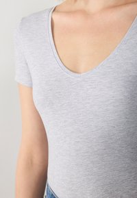 Bodysuit gris à manches courtes avec décolleté en V, fabriqué en tissu doux et texturé. La coupe slim met en valeur les contours du corps.