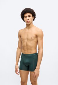 Σκούρα πράσινα μπόξερ κατασκευασμένα από λείο συνθετικό υλικό. Διαθέτουν εφαρμοστή σχεδίαση με άνετη μέση και χωρίς ορατές ραφές.