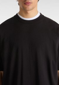 Černé bavlněné tričko s kulatým výstřihem a krátkými rukávy. Měkká textura, minimalistický design a uvolněný střih. Bílé tričko na spodní vrstvě viditelné pod ním.