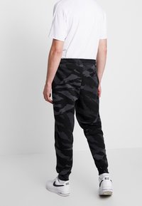 Černé maskáčové tepláky z měkké látky, s úzkým střihem, elastickým pasem a žebrovanými manžetami. Kombinovány s bílými teniskami.