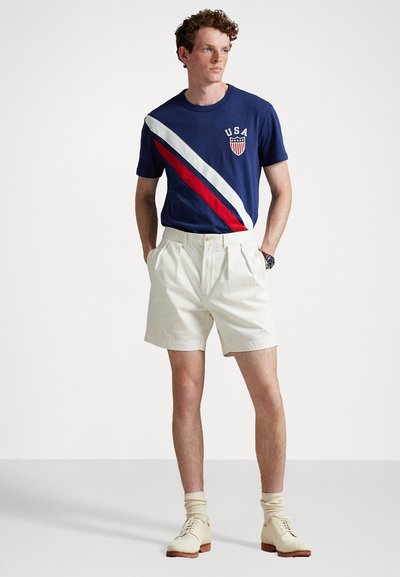 Tricou marin cu dungi diagonale roșii și albe, având logo-ul "USA" și un scut; șorturi crem; încălțăminte de culoare deschisă; șosete cu model canalé.