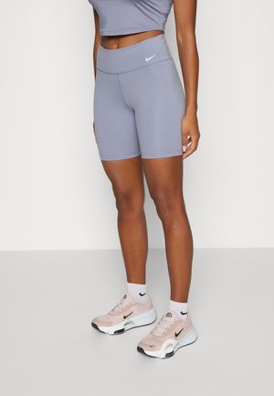 Femme portant un short de vélo taille haute violet clair, un top court assorti, des chaussettes blanches Nike et des chaussures de running Nike rose clair.